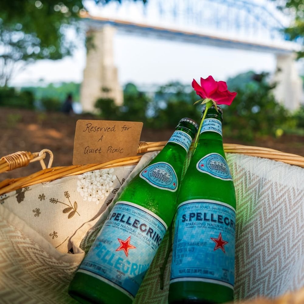 Two bottles of sparkling water and a rose in a basket, with the blue bridge across the river behind.