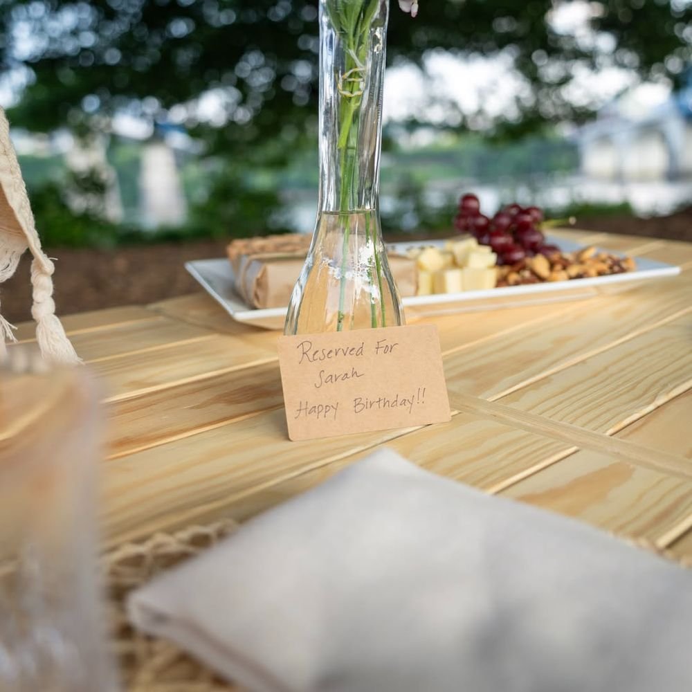 A kraft card hand-written "Reserved for Sarah, Happy Birthday" on a pine table beside a board of cheese and grapes.