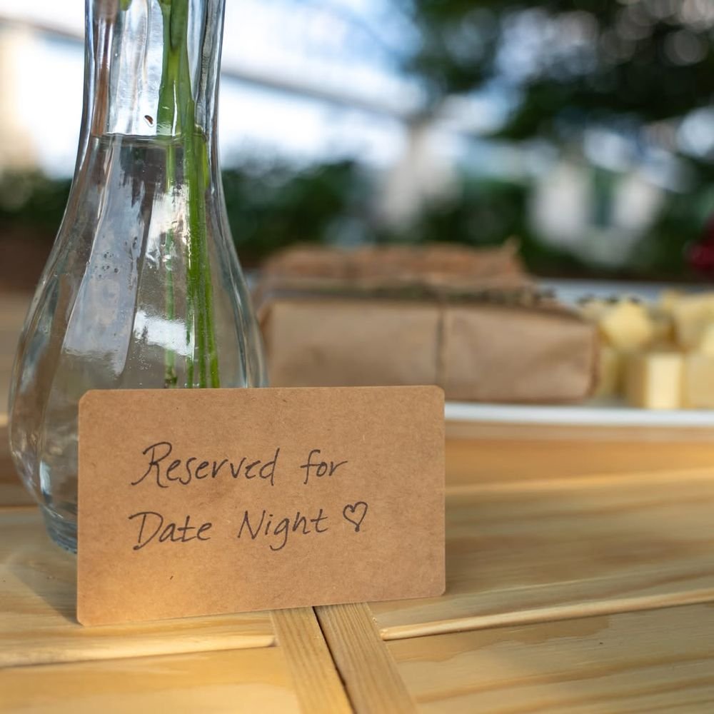 A kraft card hand-written "Reserved for Date Night" propped against a glass bud vase on a pine table.