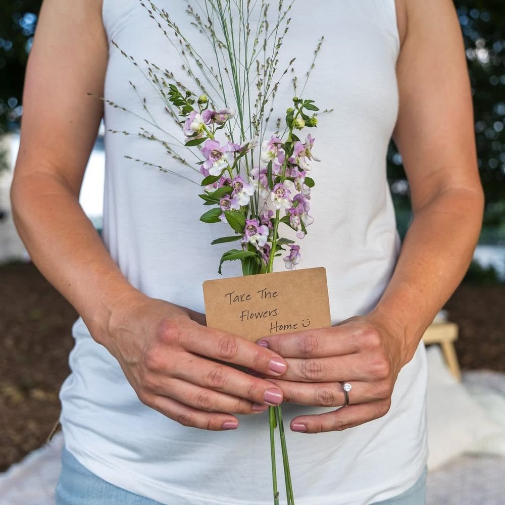 Someone holding a small bunch of pink and white flowers with a kraft card reading "Take the flowers home".
